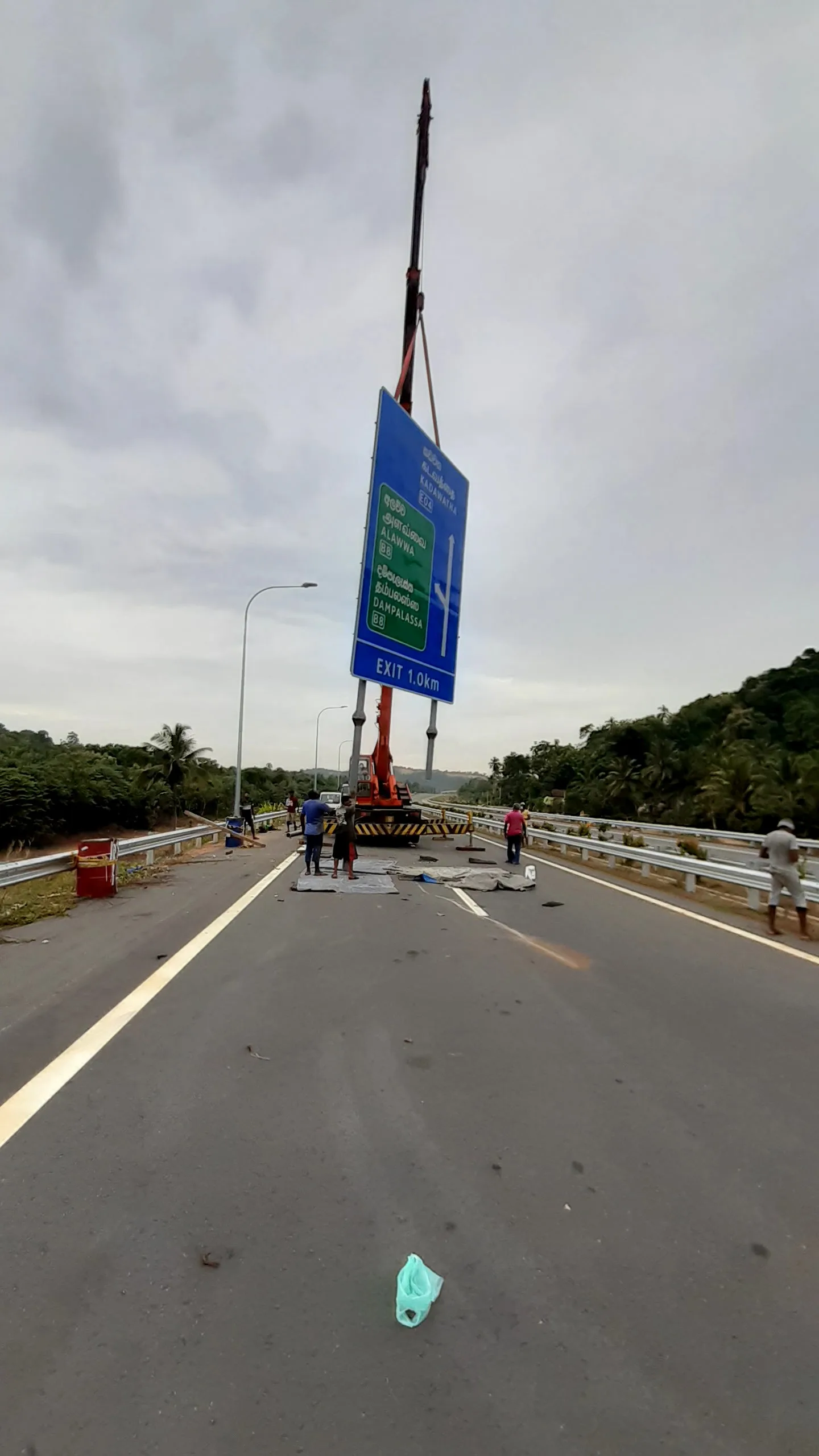 Crane hoisting large expressway exit sign board onto highway